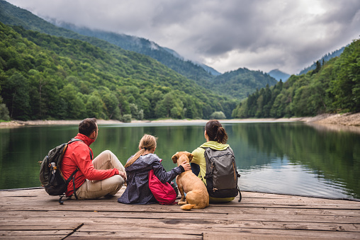 Image of family with a small yellow dog resting on a pier and looking at lake and foggy mountains